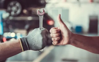 Repair worker with gloved hand and wrench getting thumbs up from a customer.