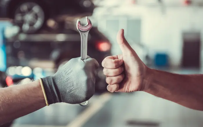 Repair worker with gloved hand and wrench getting thumbs up from a customer.